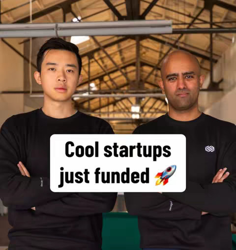 Two men with arms crossed are standing in front of open-metal beam style ceiling with a green screen in front them, with a white text bubble overlayed on them.
