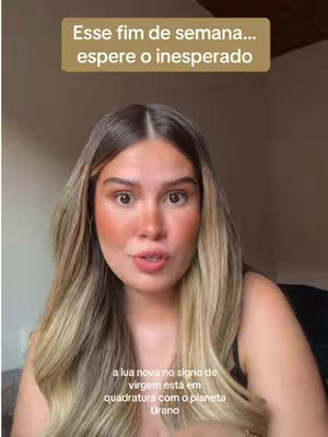 A young woman with long, wavy blonde hair is centered in the frame, looking directly at the camera. She is wearing a black top, and the background appears to be a blurred indoor setting. Overlayed on top is a text box in a light brown shade, with the text 'Esse fim de semana... espere o inesperado'. Below her, there's additional text in grey, describing the astrological event. The image has a natural lighting condition, with no hard shadows visible.