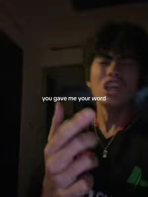 A young man in a dark setting, likely indoors, is speaking into a microphone. The camera is focused on his face and upper body, he has dark hair and is wearing a black top. Text overlay "you gave me your word" appears in white font.