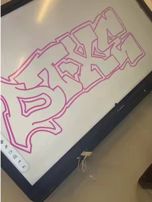 A whiteboard with a pink graffiti-style text, set at an angle against a wall. The text is outlined and appears to be a stylized word. There is a connecting cable coming out of the the wall.