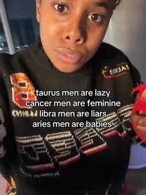 A person with dark hair and skin is centered. They are wearing a black sweater with colorful accents. Text is overlaid, listing zodiac sign stereotypes. The background is blurred, suggesting an indoor setting.