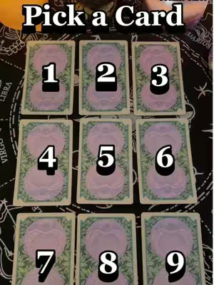The image is a top-down view of a tabletop tarot card reading setup. Nine tarot cards are arranged in a three-by-three grid. Each card's face is visible, with a large number (1-9) in bold white font over a circular design. The cards are set against a black cloth decorated with astrological symbols.