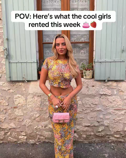A woman stands in front of a stone wall and window, wearing a two-piece floral outfit and carrying a pink purse. Text overlays are present.