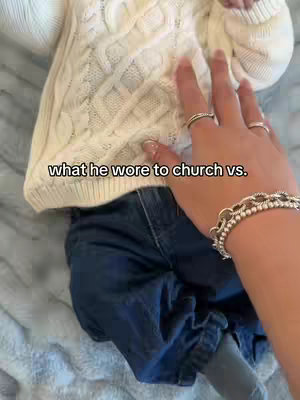 The cover image shows a close-up view of a baby wearing a white sweater and blue jeans. A hand with rings and a bracelet touches the baby's sweater. The background is a light blue, possibly a blanket.