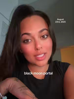 A woman with dark hair and brown eyes looks directly at the camera, with a soft, warm complexion. She is wearing a black top. Text overlays include the date at the top right ("August 23rd, 2025") and the phrase "black moon portal" at the bottom center.