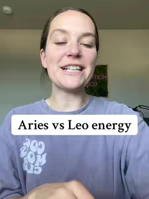 A woman with light skin and light brown hair smiles and speaks directly towards the camera. She's wearing a purple t-shirt and is set against a domestic background.