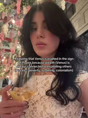 A woman with dark hair holds a cocktail, looking at the camera as text overlays the image. The background is blurred, with pink floral decorations visible. The woman wears a white lace top, and the setting appears to be a restaurant or bar.