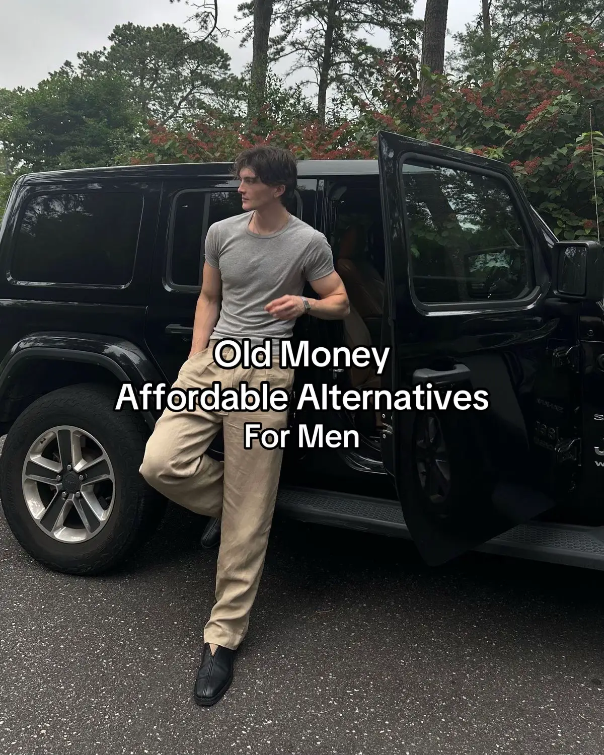 A man in neutral-toned clothing is leaning against a black SUV, with a natural background of green foliage and a cloudy sky. Text overlays read, "Old Money Affordable Alternatives For Men."