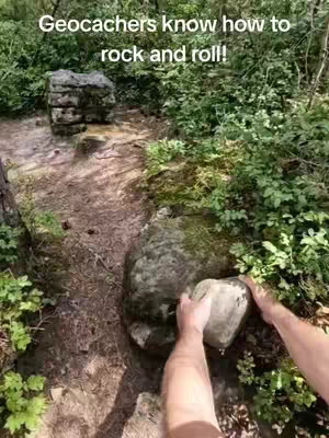 An overhead shot shows a person's hands maneuvering a rock in a forest setting. The focus is on the interaction with the rocks, emphasizing the geocaching theme. The colors are natural greens and browns. There is text at the top.