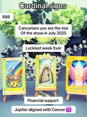 The image features three tarot cards on small wooden easels in the foreground. In the background, there are green and white flowers. Text overlays are present, including "Cardinal signs," "Cancerians you are the star Of the show in July 2025," "Luckiest week Ever," "Financial support," and "Jupiter aligned with Cancer ♋". The layout is vertical, with a soft focus on the background.