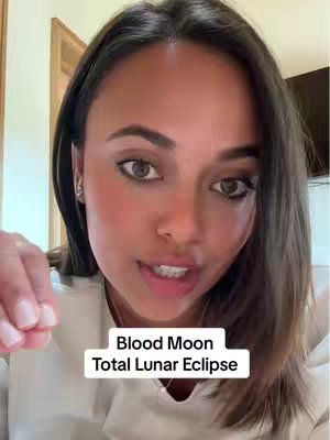 A woman with dark hair and makeup speaks directly into the camera in a close-up shot, with a text overlay at the bottom that reads 'Blood Moon Total Lunar Eclipse'. The background is a room with a wooden door frame visible.
