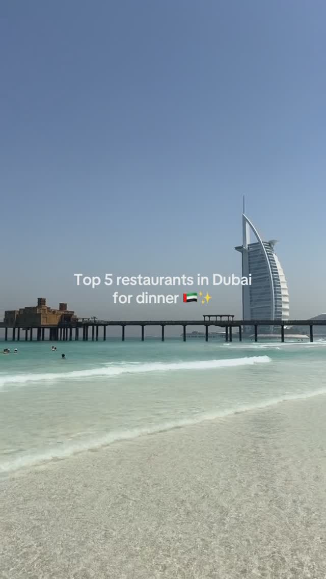 The image showcases a scenic view with a light blue sky and clear water meeting a sandy beach. A pier extends into the sea, and in the background, a modern architectural structure is visible. Text overlayed in white indicates the video's topic.