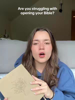 A young woman with long brown hair is holding a closed book, with text over her head. She is looking at the camera with her mouth open, as if she is speaking. The background is a blurred interior with a bed and wall visible.