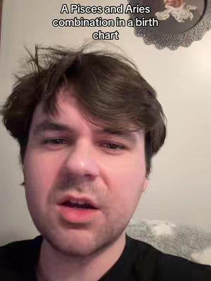 A selfie-style shot featuring a fair-skinned man with short brown hair. He is centered in the frame, with an open mouth as if he is speaking. His expression is slightly furrowed, conveying a thoughtful or serious tone. The background contains a plain wall and an element that looks like a decorative circular plate, mounted on the wall.
