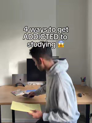 The image shows a young man standing in front of a desk, holding a yellow document and phone. Text overlaid says, "4 ways to get ADDICTED to studying". He appears to be in a home office with a computer and other items on the desk.