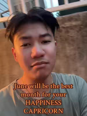 A selfie-style video image featuring a young man in a close-up shot. The background is slightly blurred, suggesting an outdoor or public setting. The man has short, dark hair and is wearing a light green t-shirt, with a gold chain around his neck. Text overlayed on the image provides astrological information.
