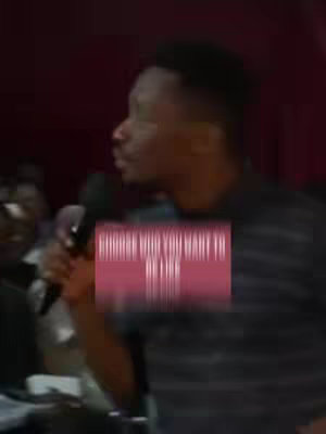 The cover image shows a man speaking into a microphone, seen from the side, in front of a blurred background. A rectangular text overlay appears at the bottom center of the image, featuring white text on a maroon background.