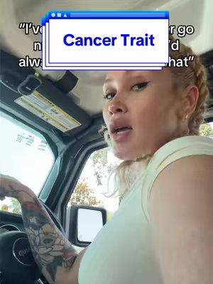 A woman with blonde hair is in a car, looking at the camera. A text overlay with a browser window design says "Cancer Trait". She's holding the steering wheel, with a tattoo visible on her arm.