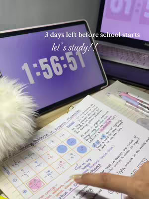 The image is a well-lit, organized workspace, likely a desk, with school materials. The central focus is on a notebook open to handwritten notes. A digital timer, displaying 1:56:51, and a laptop, are visible. The overall color scheme is soft, dominated by purples and whites.