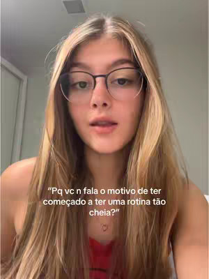 A young woman with long blonde hair wearing glasses and a red top is centered in the frame, speaking directly to the camera. Text overlayed on the image poses a question about her motivation for maintaining a busy routine. The background appears to be a simple room, with a white door visible.