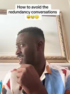 A man with dark skin is speaking in a room. He’s wearing a colorful shirt, and some text is displayed above his head.