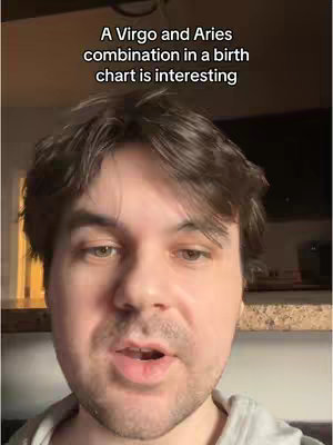 A selfie-style video cover with a man's face filling most of the frame. Above his head, in a black box, text states: 'A Virgo and Aries combination in a birth chart is interesting'. The man has brown hair and is looking and speaking towards the camera. The background is blurred, revealing a home setting. The color palette is neutral with warm lighting.