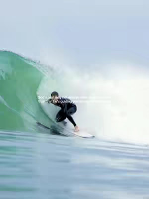 The image is a dynamic shot of a surfer riding a wave. The surfer, clad in a black wetsuit, is positioned in the wave's crest. The wave itself is a vibrant green, contrasted against the blue of the water and the sky above. Text overlayed on the image reads a quote about God's plan.