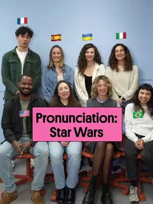 A group of people of various ages and ethnicities are sitting or standing in front of a light blue background. Flags of different countries are placed above the heads of some of the people. In the center is a pink rectangle with the text "Pronunciation: Star Wars".