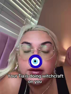 The cover image features a close-up of a person's face, with eyes closed and a blue and white eye symbol overlaying the nose. The person is wearing glasses and has light-colored hair. Text at the bottom reads, "Your Tia is doing witchcraft on you". The background has a textured appearance.