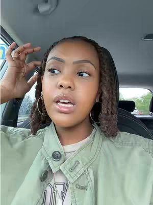 A woman with brown skin and braids is the focus, set in a car. She wears a light green jacket over a t-shirt, with large hoop earrings. The background subtly shows the car interior.