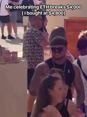 A group of people are gathered outdoors, with a man in the foreground wearing sunglasses and a black vest. He is smiling, and there is text overlayed on the image.
