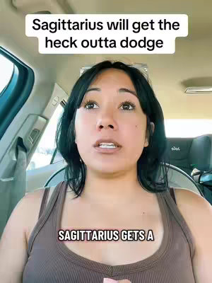 A woman with dark hair is seated behind the wheel of a car, looking towards the upper-right of the frame. Two text overlays: 'Sagittarius will get the heck outta dodge' is above her, and 'SAGITTARIUS GETS A' appears at the bottom. The woman is wearing a brown tank top. The car's interior is visible, with the door and dashboard partially in view, along with the side view of the seat behind her.