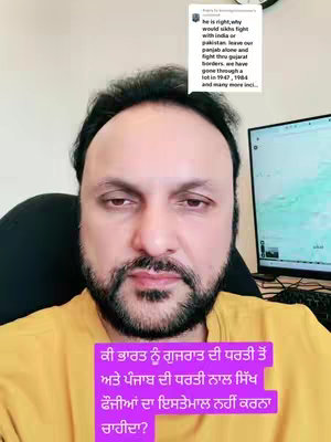 A man with dark hair and a beard looks at the camera with a neutral expression. He is wearing a yellow shirt, and there is text over the bottom half of the shot. A monitor and other office equipment are visible in the background.