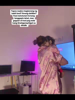 A woman is holding a child close to her chest, with the child's face partially visible. The woman is wearing a pink floral-patterned robe. The background shows a room with a television, a desk with electronic devices, and a white wall. Text overlaid on the top left reads in a paragraph touching on accepting difficult facts about her child.