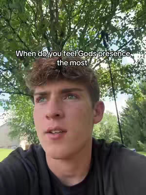 A young man with brown hair and blue eyes looks directly at the camera. The background includes lush green foliage, likely a tree, and a partly visible building. Text overlay at the top reads, 'When do you feel Gods presence the most'.