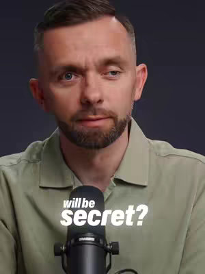 A medium shot features a man with fair skin, a short beard, and short, dark hair. He appears to be speaking, with a microphone positioned in front of him. The overlaid text reads "will be secret?" in white font. The background is a dark gray, making the man and the text stand out. He is wearing a light green button-up shirt.