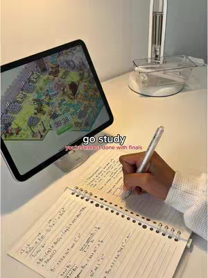 A desk scene with a tablet displaying a game, a notebook with handwritten notes, and a hand holding a pen. The color palette is neutral with soft lighting.