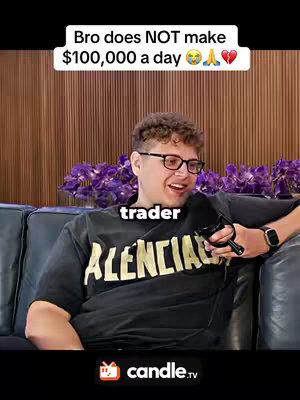 A man with curly hair and glasses sits on a black couch, holding a microphone. A text overlay says, "Bro does NOT make $100,000 a day πππ". Behind him are purple flowers, and the background features brown vertical planks. The man is wearing a dark t-shirt with "BALENCIAGA" in large yellow letters. He has a watch on his wrist.