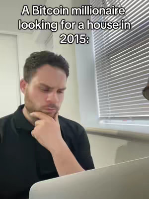 A man with short dark hair is shown in a partial view, with a thoughtful expression. He's seated indoors, presumably in an office or home setting, looking down at a laptop computer, hand on chin, and appears to be contemplating something. The background includes a window with vertical blinds and a portion of a lampshade. Above the man, text is overlaid.