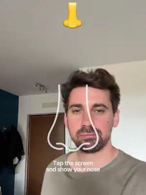 A selfie-style video cover image featuring a man's face with a white outline of a nose and the prompt "Tap the screen and show your nose." Above his head is the emoji of a yellow nose.