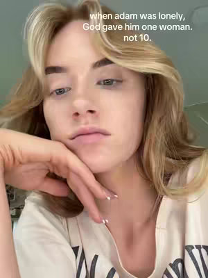 A selfie-style shot with a light-skinned woman as the central focus. She has long, light-colored hair and is wearing a neutral-colored shirt. Her hand is gently touching her face at her jawline. Overlayed text in white font appears at the top, partially obscured by her hair, against a pale background that's part of a domestic setting.