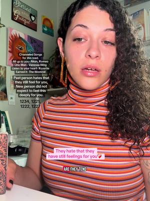 A woman with curly dark hair poses for a selfie. She wears an orange and white striped turtleneck and gold hoop earrings. Text overlays appear in the image, including a series of channeled messages and phrases. The background features framed art pieces.