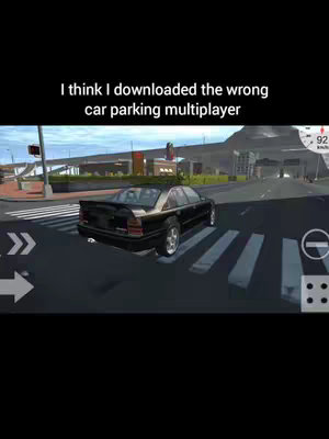 The cover image is a screenshot from a mobile game, featuring a black sedan car on a road with crosswalk markings. The car is positioned on the left side of the screen, with the rear of the vehicle facing the viewer. In the background, there are city buildings and a road with traffic lights, suggesting an urban environment. On the right side of the screen, there are on-screen game controls. The title overlayed over the image says, "I think I downloaded the wrong car parking multiplayer".