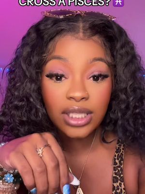 A young woman with long, dark curly hair is centered in the frame, looking directly at the camera. She has professionally applied makeup including eyeshadow and long eyelashes. She is wearing a patterned top. Sunglasses are perched on top of her head. Her left hand is near the screen, revealing a ring.