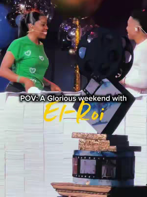 A vertical shot capturing a live stage event. Two women are on the left side, one in a green shirt, both looking towards the right, where a decorative object dominates the scene, possibly a large, ornate structure. The lighting suggests an indoor setting, potentially a conference or a performance.