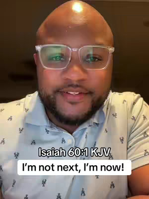 A medium close-up of a Black man wearing square, clear-rimmed glasses and a light blue button-down shirt with a pattern of small white lobsters. The man has a partially bald head and a short beard. The image has a well-lit, indoor studio appearance, with a simple background.