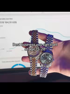 A hand holding two luxury wristwatches in front of a monitor displaying financial data. The watches are positioned center, and the background suggests an office or financial setting. The overall composition is well-lit, with a focus on both the watches and the data.