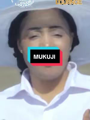 A person is centered in the frame, the top of their head is covered by a circular white hat. The person's facial expression is neutral. A brightly colored rectangle covers the center of the face, displaying the word 'MUKUJI' in a bold, sans-serif font.