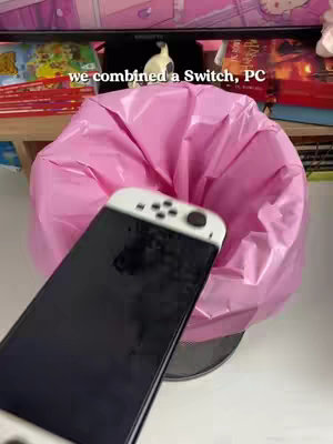 The image shows a Nintendo Switch console, with the screen facing away, over a pink garbage bag inside a black wastebasket. The text overlay at the top reads "we combined a Switch, PC". In the background, a desk, a monitor, and some decorations are visible