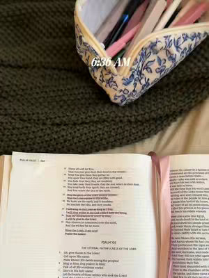 The image shows an open Bible with a pink ribbon bookmark. A pencil case with blue floral pattern sits on top. The background is a green knitted blanket. At the top of the image is the text "6:36 AM".